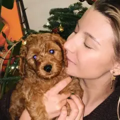 Słodki piesek Julii Wieniawy, rudy szczeniak, przytula się do swojej pani na tle świątecznej choinki.